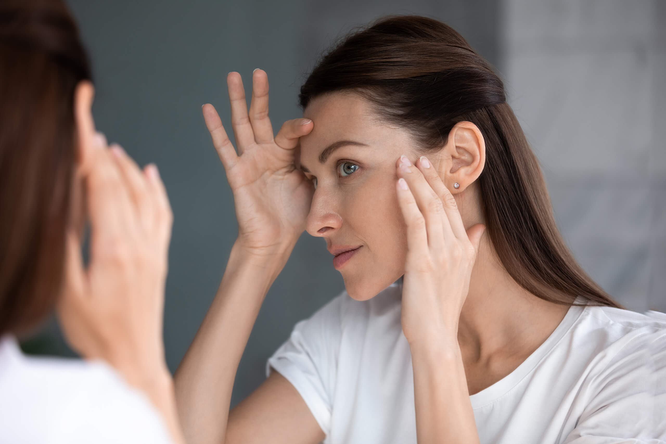 A woman inspects her face in a mirror as she considers a facelift.