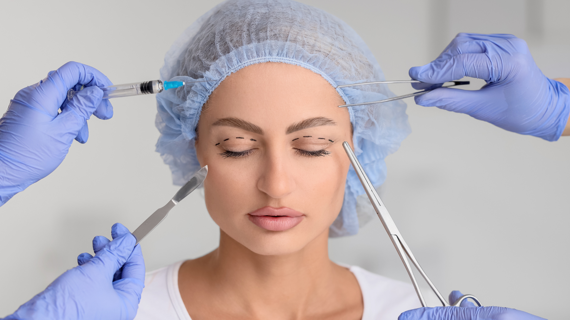 A person with her eyes dotted and closed while hands with gloves hold surgical tools around the face.